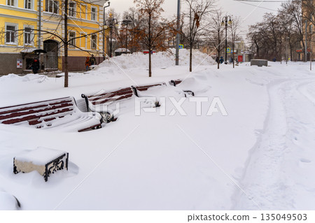 After snowstorm in city. Snow covered benches in city park almost fully buried after record snowfall near residential area. Concept of climate change, failed maintenance, urban winter paralysis After snowstorm in city. Snow covered benches in city park almost fully buried after record snowfall near residential area. Concept of climate change, failed maintenance, urban winter paralysis 135049503