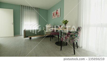 Modern minimalistic bedroom with green walls, floral chairs, and cozy atmosphere. Beds beside large window with sheer curtains letting in light. Stylish table setting with flowers enhancing the room's 135050210