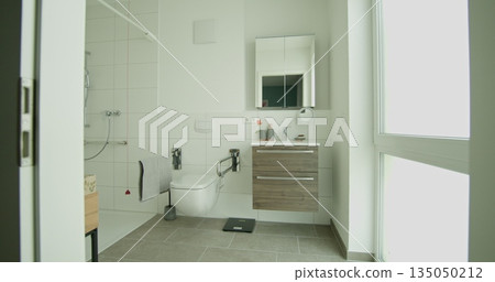 Contemporary bathroom with wheelchair accessible shower and modern vanity. White tiles and natural light create clean and bright space. Design includes accessible features for ease of use. 135050212