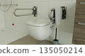 Modern bathroom featuring wall-mounted toilet, safety support bars, and towel. Accessible and functional design promoting independence and safety 135050214