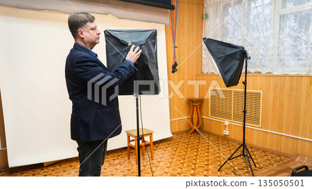 Photographer turning on softbox lighting equipment in a professional photo studio setup for portrait or product photography 135050501