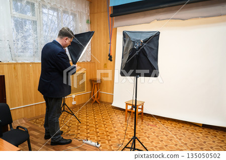 Photographer turning on softbox lighting equipment in a professional photo studio setup for portrait or product photography Photographer turning on softbox lighting equipment in a professional photo studio setup for portrait or product photography 135050502