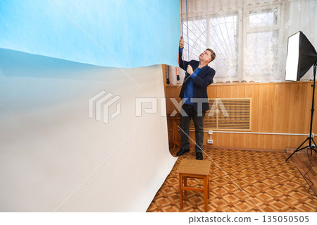 Photographer raising a blue backdrop for a portrait photography session in a professional photo studio Photographer raising a blue backdrop for a portrait photography session in a professional photo studio 135050505