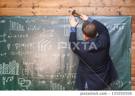 Photographer hammering a themed backdrop onto the wall for a school-themed photo session in a studio Photographer hammering a themed backdrop onto the wall for a school-themed photo session in a studio 135050508
