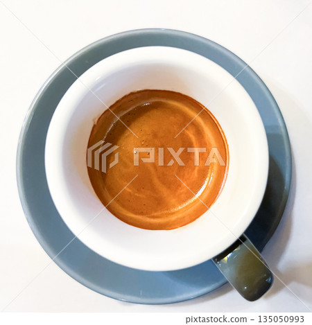 Top view of a cup of fresh espresso with rich crema on white background, minimalist flat lay coffee composition, morning caffeine and cafe concept Top view of a cup of fresh espresso with rich crema on white background, minimalist flat lay coffee composition, morning caffeine and cafe concept 135050993