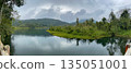 Panoramic view of a tropical mountain lake surrounded by lush green forest and hills, calm water reflections under cloudy sky, peaceful nature landscape 135051001