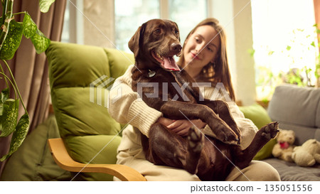 Woman holding dog in her arms while sitting on sofa at home Woman holding dog in her arms while sitting on sofa at home 135051556