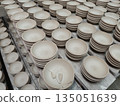 Rows of stacked unglazed ceramic bowls drying on shelves in pottery workshop showing traditional craft production with raw clay texture and neat arrangement waiting for kiln firing process 135051639