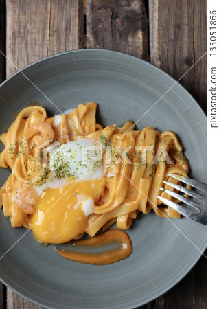 A rich shrimp cream pasta with flat noodles topped with a crumbled soft-boiled egg 135051866