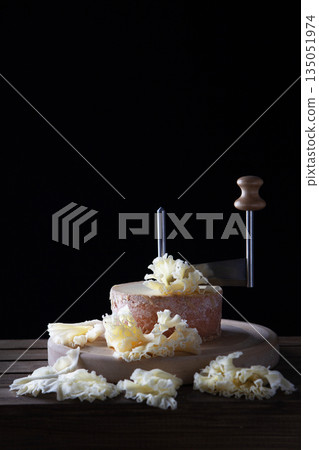Traditional aged Tete des Moines cheese on wooden board. Black background. Special knife for slicing cheese "Girol".Copy space. 135051974