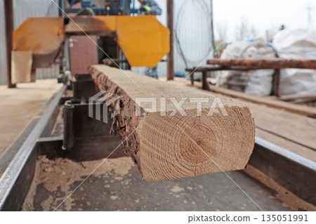Sawing of wooden logs. The log is sawn on a machine. A woodworking machine. Wood processing workshop. Carpentry work. 135051991