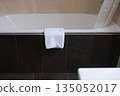 A foot towel is hanging on the edge of the tub. Bathroom. White terry towel. The concept of cleanliness and order. 135052017