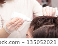 A cosmetologist applies a hair restoration product to the scalp. Hair care. A remedy for the treatment of the scalp. A woman takes care of her hair in a beauty salon. The problem of dry hair. 135052021