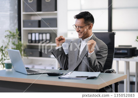 Happy male businessman celebrating success, raising hands in excitement Happy male businessman celebrating success, raising hands in excitement 135052083