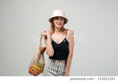 Woman posing with reusable textile shopping bag and fresh groceries, sustainable living and eco friendly consumption concept in studio Woman posing with reusable textile shopping bag and fresh groceries, sustainable living and eco friendly consumption concept in studio 135052165