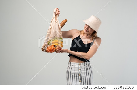 Smiling woman presenting reusable mesh bag with fresh food, eco shopping and sustainable lifestyle concept with copy space 135052169