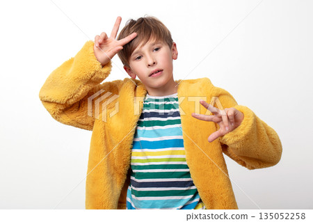 A boy wearing a yellow jacket and striped shirt. He is making a peace sign with his hands 135052258