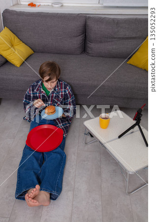 Child enjoying snack while sitting on the floor in cozy living room with a table and tripod in afternoon light 135052293