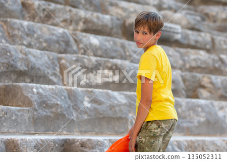Tired teenage boy looking at camera on iPhone on steps of amphitheater. Tired teenage boy looking at camera on iPhone on steps of amphitheater. 135052311