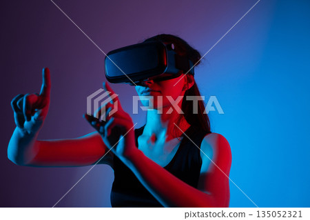 Woman in virtual reality headset controlling digital interface with dual finger gestures 135052321