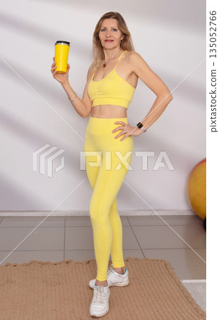 Woman in yellow athletic wear holding a drink in a fitness studio during a workout session Woman in yellow athletic wear holding a drink in a fitness studio during a workout session 135052766
