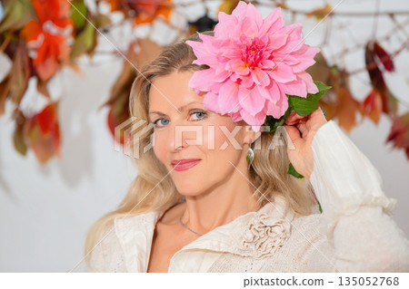 Woman with a large pink flower in her hair poses cheerfully in front of colorful autumn leaves Woman with a large pink flower in her hair poses cheerfully in front of colorful autumn leaves 135052768