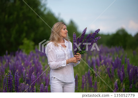 Woman holding fresh lupine flowers in a blooming field during daytime Woman holding fresh lupine flowers in a blooming field during daytime 135052779