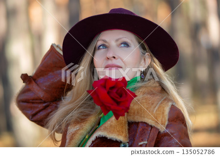 Woman in brown coat with red rose posing in forest 135052786
