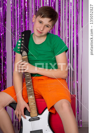 Young boy poses with electric guitar in vibrant setting while wearing colorful outfit at a cheerful event 135052827