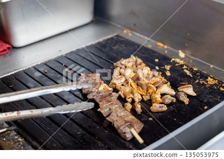 A person is cooking anticuchos on a grill A person is cooking anticuchos on a grill 135053975