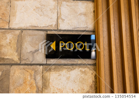 Directional pool sign mounted on stone wall indoors. Clear wayfinding design, guest orientation, and functional hospitality communication enhancing relaxed resort navigation. Directional pool sign mounted on stone wall indoors. Clear wayfinding design, guest orientation, and functional hospitality communication enhancing relaxed resort navigation. 135054554