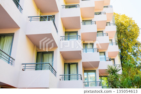 Repetitive balconies on modern building facade with soft pastel tones. Architectural rhythm, urban living aesthetics, and structured design shaping contemporary residential environments. 135054613