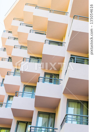 Repetitive balconies on modern building facade with soft pastel tones. Architectural rhythm, urban living aesthetics, and structured design shaping contemporary residential environments. Repetitive balconies on modern building facade with soft pastel tones. Architectural rhythm, urban living aesthetics, and structured design shaping contemporary residential environments. 135054616