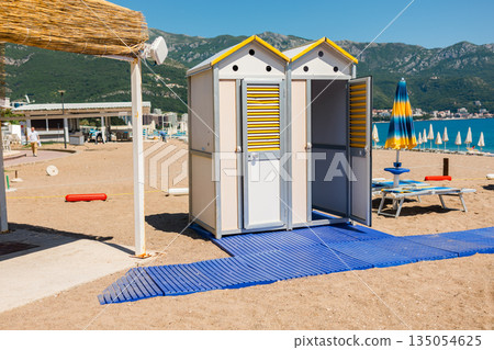 Beach changing cabins with accessible walkway near seaside shore. Coastal infrastructure, inclusive design, and practical services supporting comfortable summer recreation. 135054625