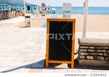 Empty blank restaurant menu board placed near beach promenade. Hospitality marketing, visual communication, and seaside dining promotion supporting tourist oriented food services. Copy space 135054652