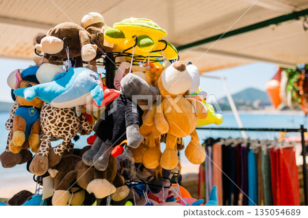 Plush animal toys hanging at seaside souvenir. Children merchandise, tourism retail, playful design, and colorful coastal market scene Plush animal toys hanging at seaside souvenir. Children merchandise, tourism retail, playful design, and colorful coastal market scene 135054689