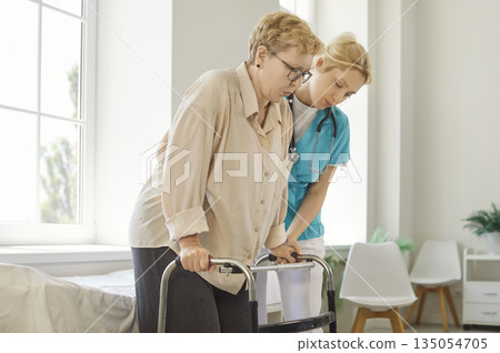 Support and help from nurse to elderly patient learning to walk with walker Support and help from nurse to elderly patient learning to walk with walker 135054705