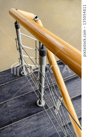 Modern indoor staircase with polished wooden handrails, metal banisters with wire cables, and dark stone steps 135054811