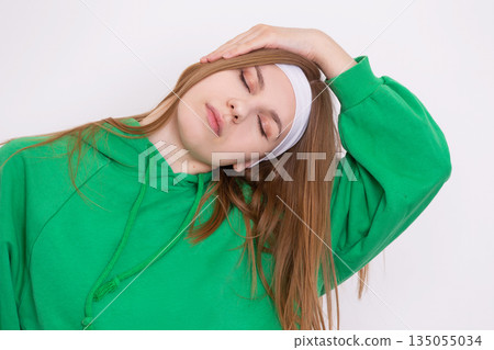 Relaxation exercise for neck strain in green hoodie with headband indoors Relaxation exercise for neck strain in green hoodie with headband indoors 135055034