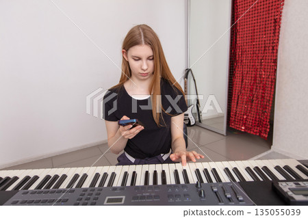 Young musician practices keyboard while checking phone in modern music studio space Young musician practices keyboard while checking phone in modern music studio space 135055039