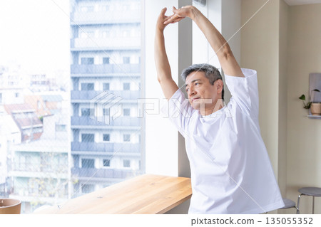 一位老人在窗邊伸展身體。 135055352