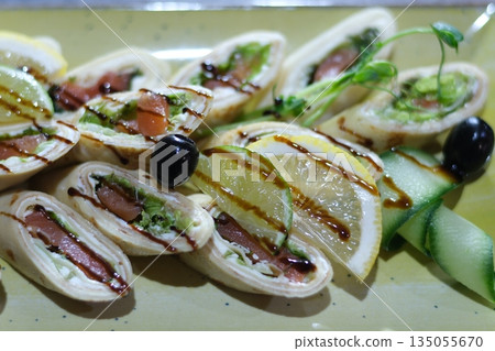 A beautifully arranged platter showcases thinly sliced rolled meats, garnished with fresh herbs and colorful fruits. Ideal for serving at gatherings or special occasions to impress guests. 135055670