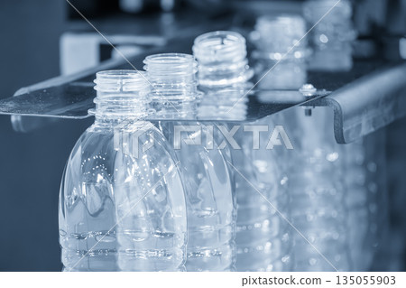 The empty drinking water bottles on the conveyor belt for filling process in the light blue scene. The empty drinking water bottles on the conveyor belt for filling process in the light blue scene. 135055903