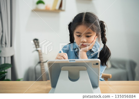 Asian girl using digital tablet with stylus pen for online learning or drawing at home. Cute kid studying with technology, creative art and smart education concept. 135056884