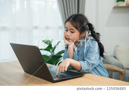 Bored Asian girl using laptop for online learning at home. Tired kid sitting at table, feeling stressed or lazy with homework, studying on computer. Bored Asian girl using laptop for online learning at home. Tired kid sitting at table, feeling stressed or lazy with homework, studying on computer. 135056885