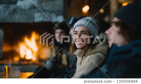 Group of happy young adult friends enjoying warm relaxed moments ski, sitting by a cozy fireplace in a rustic lodge during winter holidays 135056994