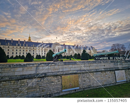 Paris, France - December 09, 2025: Les Invalides at sunset, with the Army Museum behind historic cannons. Beautiful view to the grand courtyard, stone walls, and manicured hedges under a vibrant sky 135057405