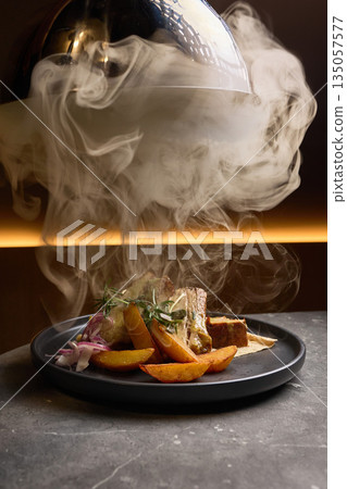 Appetizing smoked dish with roasted potatoes, decorated with rosemary on dark plate, steam rising elegantly, fine dining concept Appetizing smoked dish with roasted potatoes, decorated with rosemary on dark plate, steam rising elegantly, fine dining concept 135057577