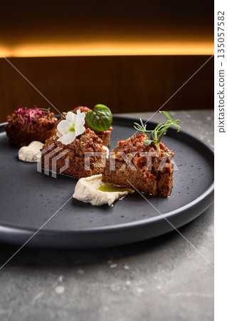 Gourmet appetizer, rye bread pieces with flavorful toppings, garnished creatively, served elegantly on black plate, fine dining concept Gourmet appetizer, rye bread pieces with flavorful toppings, garnished creatively, served elegantly on black plate, fine dining concept 135057582