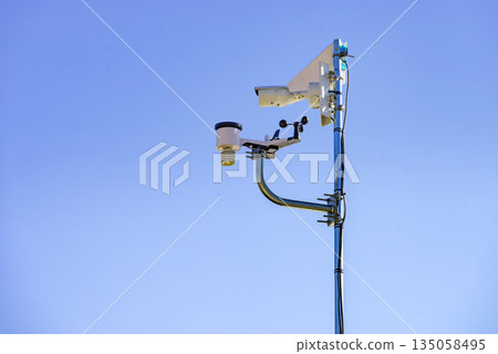 Security video camera and wind indicator against sky. Security video camera and wind indicator against sky. 135058495